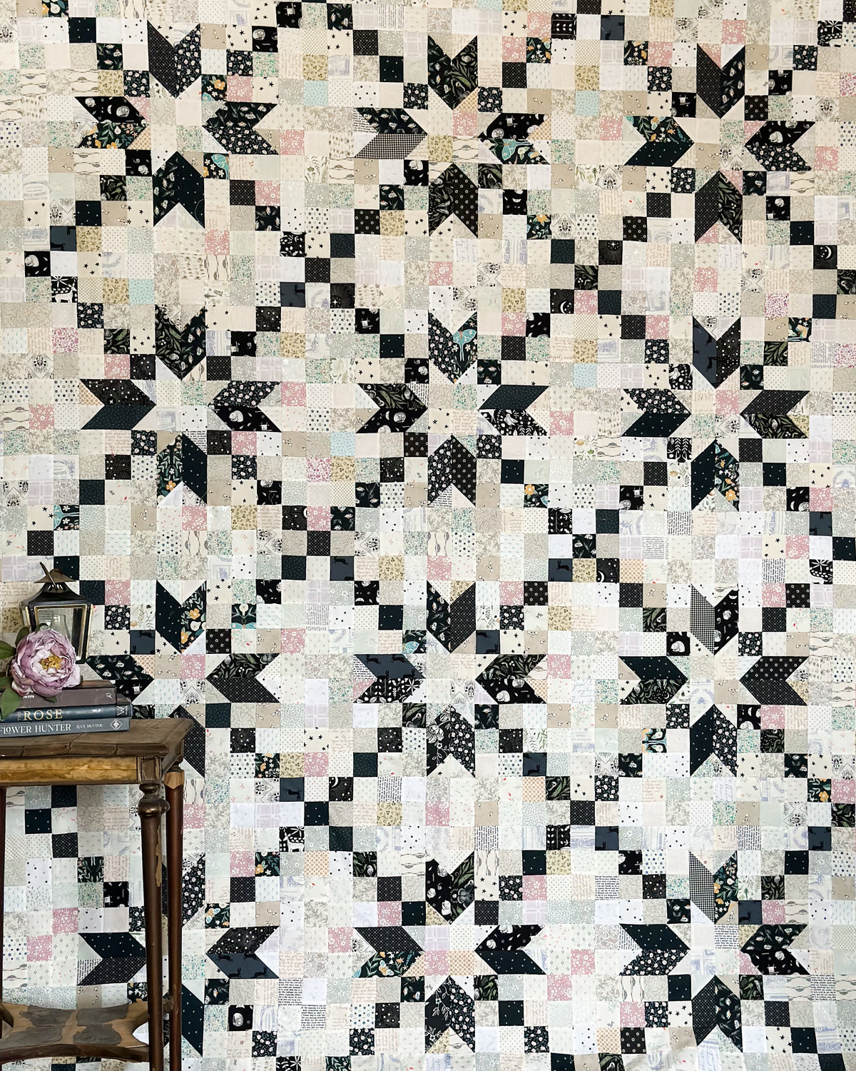A quilt with a geometric patchwork design in black and white, displayed on a wall.