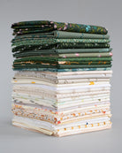 A tall stack of folded patterned fabrics in various colors and designs, including greens, creams, and florals, photographed against a neutral gray background.