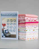 A quilt pattern book titled 'DENIM & LACE' stands next to a tall stack of folded quilts in various pink, white, and patterned designs on a neutral gray background.