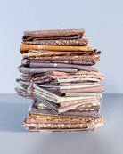 A stack of folded quilting fabrics in earthy brown, beige, and gray patterns, wrapped in clear plastic and tied with a string, set against a light gray background.