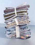 A stack of folded fabric pieces bundled together with a white elastic band, photographed on a light gray surface against a pale blue-gray background.