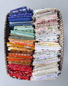 A large woven basket filled with neatly folded fabrics in a variety of colors and patterns, arranged in two columns against a plain light gray background.