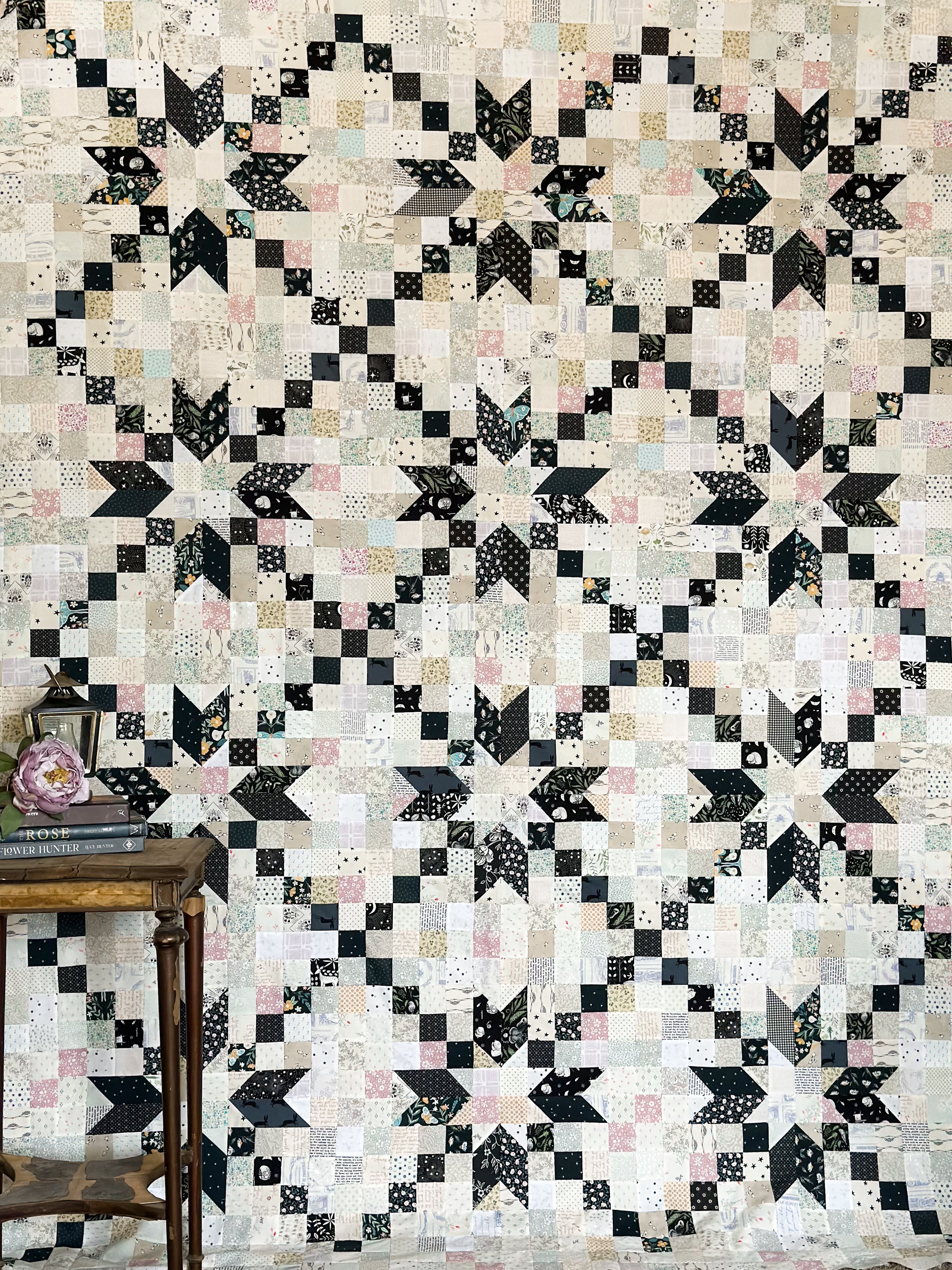 A quilt with a geometric patchwork design in black and white, displayed on a wall.