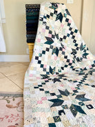 A patchwork quilt draped over a wooden stand in a home interior, featuring a mix of floral, geometric, and solid fabric blocks in cream, navy, pink, and green tones.